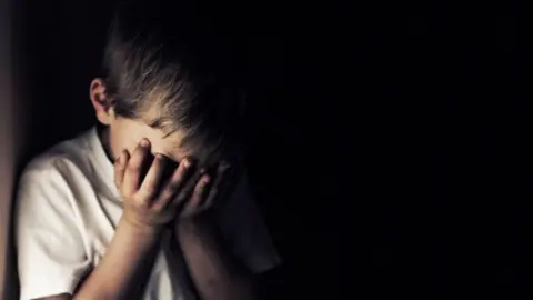 Getty Images An image of a sad child, head in hands