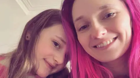 Headshot of mum Caroline and daughter Scarlett smiling into the camera - Scarlett has brunette hair while her mum has bright pink hair