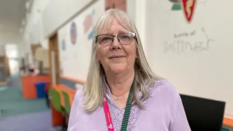 A woman with long, light hair, wearing a lilac top