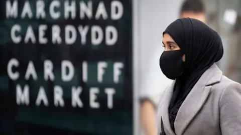 Getty Images Woman walks by Cardiff market sign, wearing face mask