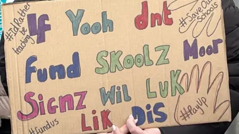 Placard with spelling mistakes suggesting unless schools get funding people won't be able to spell