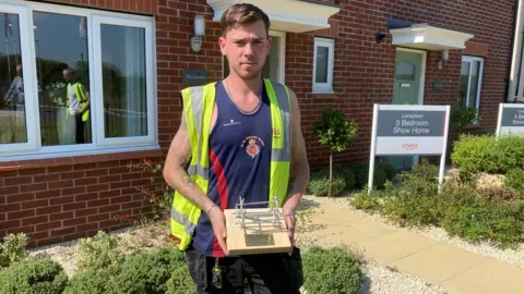 Former Grenadier Guard, Jack Aldis, holds his presentation plaque that includes scaffolding poles in honour of his new career