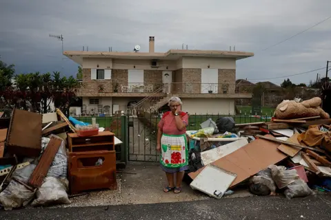 Louisa Gouliamaki / Reuters Anastasia Tsagkarakaki, 60, stands by her belongings outside her flooded house after a storm