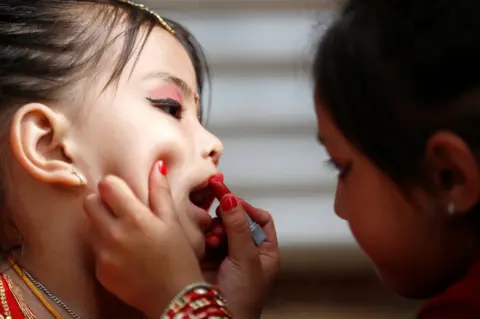 Navesh Chitrakar/Reuters A young girl applies a lipstick on her friend's lips.