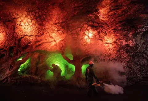 Juan Barreto / AFP Workers disinfect a salt cavern covered in carvings and lit in red and green