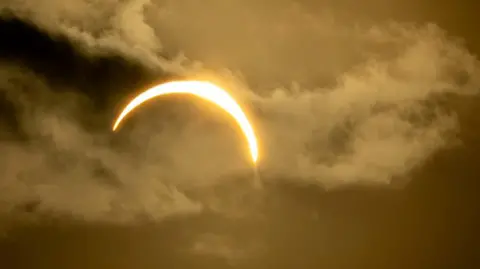 Barrie0 The sun partially eclipsed by the moon in a dark, cloudy sky