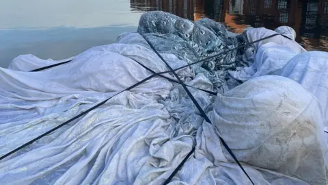 Bridgwater Town Council A deflated moon art installation, resembling a large pale cloth, floats on top of a river