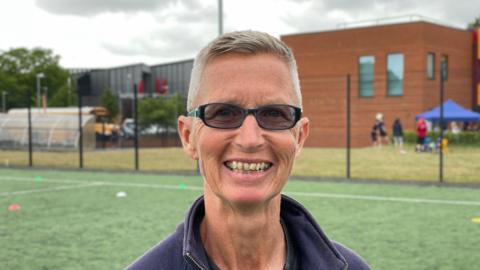 Caroline Pike smiling and wearing sunglasses on football pitch.
