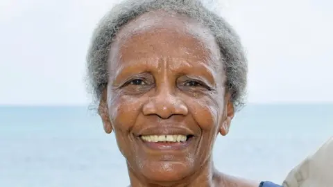 City of Wolverhampton Council A woman with grey hair looking at the camera smiling. The sky and sea are in the background.