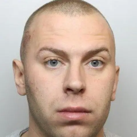 BBC Police mugshot of Cameron Evans, who has blue eyes and shaved brown hair.