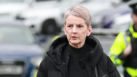PA Media A woman with cropped short grey hair.
She is walking through a car park wearing a black coat and black high necked top.