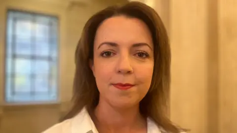 Liz Kimmins has short dark hair and is wearing makeup. 