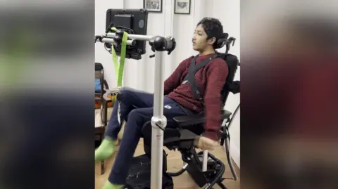 Bob Sagoo Image of a young man with black hair in a wheel chair who is looking at a screen.