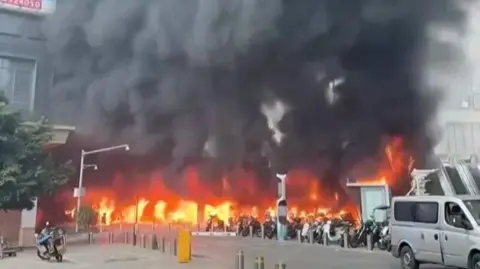 Motorcycles on fire in parking lot with black smoke billowing into sky