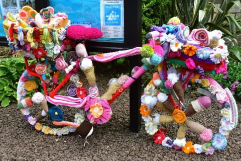 Sylvia Watson A bicycle covered in bright knitted flowers.
