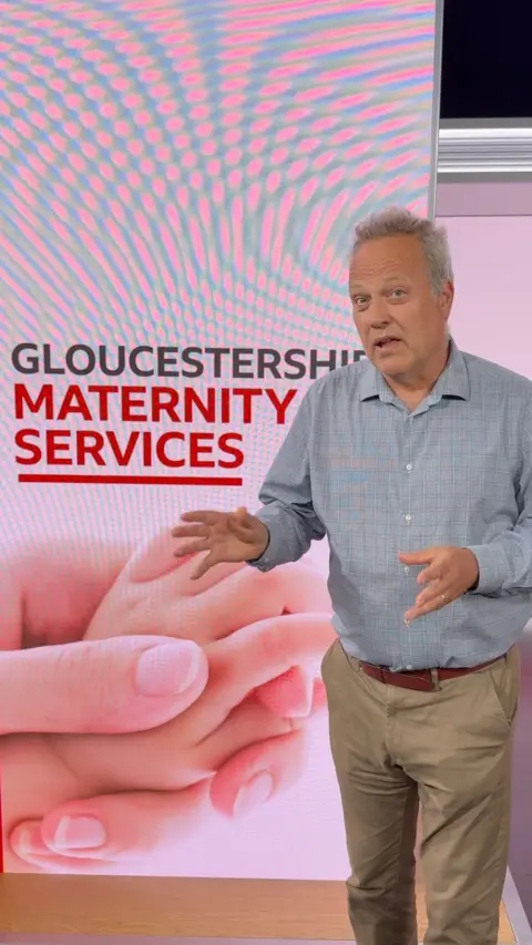 A man stands next to a large screen that has "Gloucestershire maternity services" on it