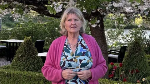 Carol Peet Carol Peet, founder of a buying agency, in a flowery dress, with a hedge and trees behind her