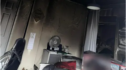 Sherianne Wood A fire-damaged bedroom, showing the walls and various items blackened by the smoke such as a fan, clothes and a sign which says "game zone".
