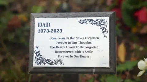 John Fairhall/BBC A silver plaque on the grave reads: 
"Dad, 1973-2023.
Gone from us but never forgotten, Forever in our thoughts, Too dearly loved to be forgotten, Remembered with a smile, Forever in our hearts."