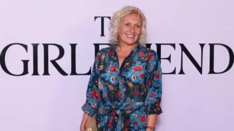 A blonde woman wearing a colourful dress. 