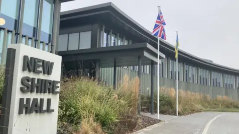 Brian Farmer/BBV Building with sign that reads "New Shire Hall" and flags outside