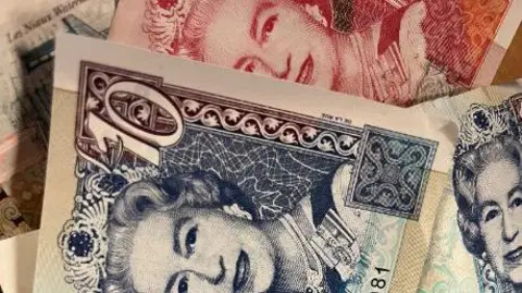 Queen Elizabeth II's face is shown on blue £10 notes and red bank notes. She is smiling and wearing a crown.