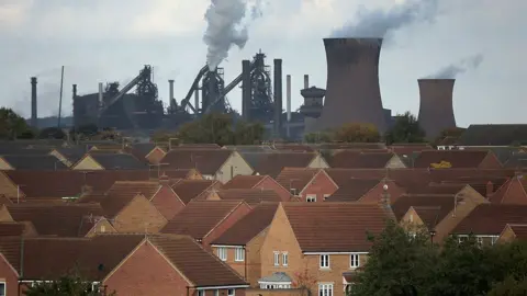 View over the rooftops of houses in Scunthorpe looking towards the smoking chimneys of the town's steelworks