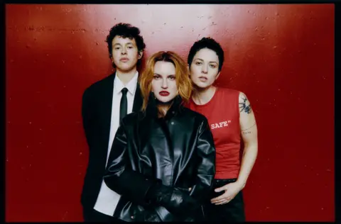 Dean Bradshaw Promotional photo of Muna, standing against a blood red wall