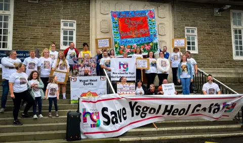 BBC Protestsor wearing white shirts and holding a banner saying save ysgol heol goffa