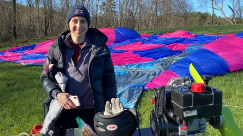 PA Media Alicia Hempleman-Adams standing in a field in front of a deflating hot air ship with her thumb up and smiling