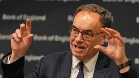 Reuters Bank of England Governor, Andrew Bailey gestures with his hands as he speaks at a Bank of England meeting in July. He has short dark hair, and is wearing glasses, a dark suit and tie.