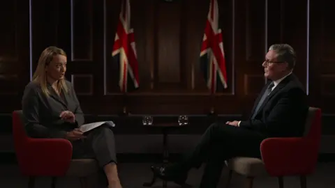 Sir Keir Starmer sits opposite interviewer Laura Kuenssberg. Two UK flags are noticeable in the distance
