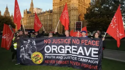 PA Media A group of people are stood outside the House of Commons with a large banner and large red flags 