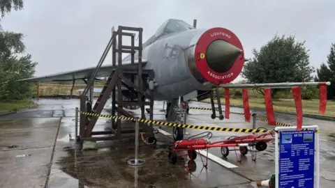 Lightning jet XR724 restoration with 'Lightning Association' on the front with tape around it and stairs going up to it 