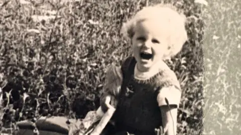 Maggie O'Farrell black and white photo of Maggie as a toddler blonde hair -- mouth open kneeling down on the ground rugged landscape of Ireland behind her
