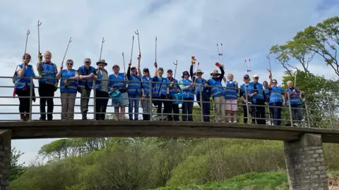 Northumberland Coast National Landscape A row of people all holding litter pickers standing on a bridge 