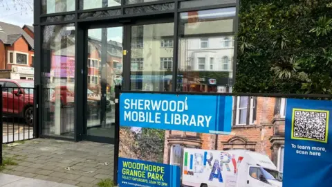 Front of new Sherwood library. Full glass windows and tall fake green flower wall.