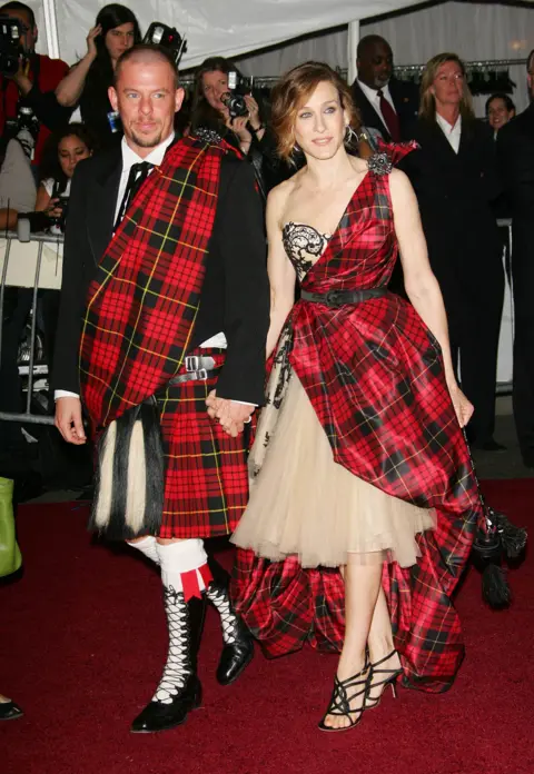 Getty Images Sarah Jessica Parker with designer Alexander McQueen. Parker is wearing a dress, mostly of red and black tartan with a nude tulle skirt. McQueen wears a kilt and plaid of the same tartan.