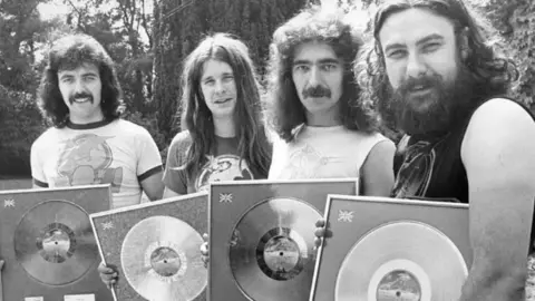 Getty Images Four men holding records looking into the camera smiling. 