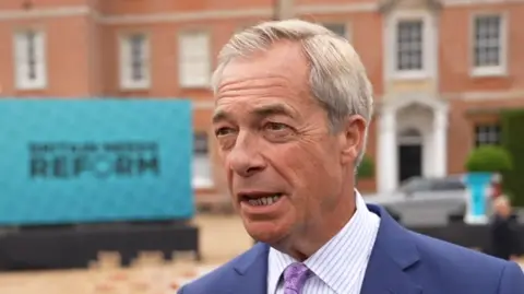 Qays Najm/BBC A man wearing a suit. His blazer and a purple tie and white striped shirt.
He is speaking to the camera.