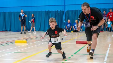 Family Handout Jake is running in a gym with a man next to him cheering him on.