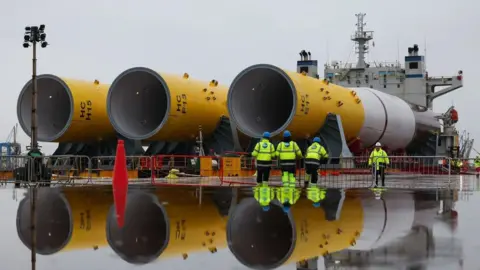 Orsted Monopiles arriving ready to be taken to Swardeston for installation. There are four people wearing hi-vis jackets and helmets in the picture which puts into perspective how big the monopiles are.