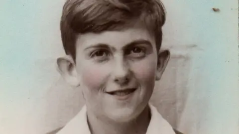 Family Handout Black and white photograph of a smiling young boy with short dark hair wearing a white shirt and a blazer.