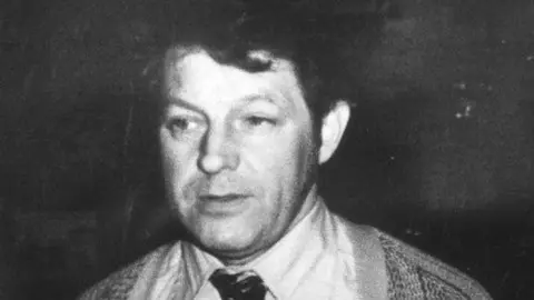 PA Media A black and white image of a man with dark hair. He is wearing a cardigan and a shirt and tie.