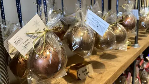 A row of hand decorated chocolate baubles on a shelf. They are wrapped in a clear cellophane wrap.