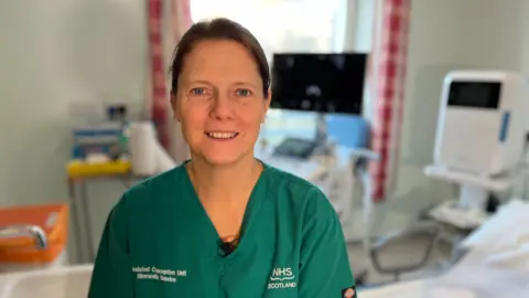 Head and shoulders image of Dr Sarah Martins Da Silva. She is wearing a green hospital tunic and looking straight at the camera. Her dark brown hair is tied back.