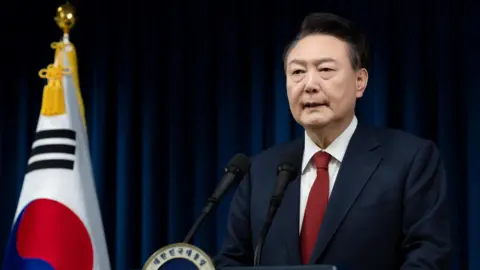 President Yoon speaking at a lectern, with the S Korea flag next to him