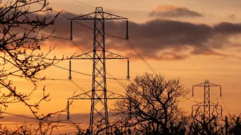 High voltage power lines running through countryside underneath an orange sky.