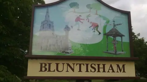 Bluntisham village sign - showing skaters and a church