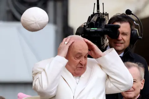 FRANCO ORIGLIA / GETTY IMAGES The cap of Pope Francis is blown off his head